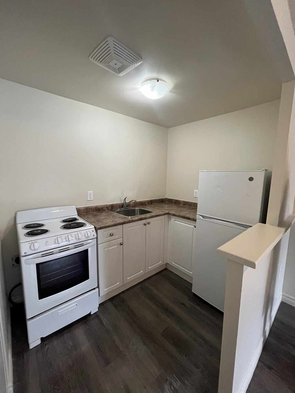 A white stove and refrigerator in a kitchen with wood floors.