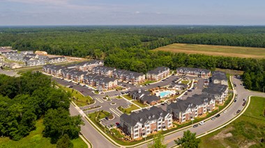 Overhead view of apartment buildings, clubhouse and pool; community is surrounded by trees and grass