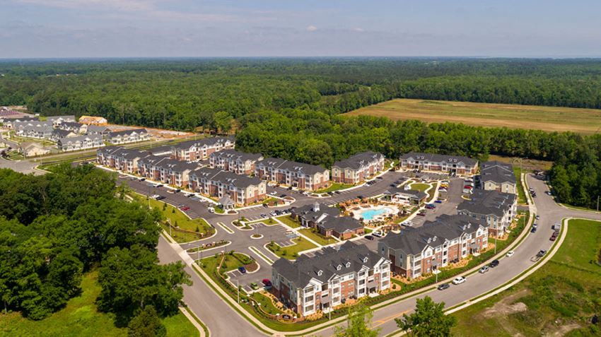 Overhead view of apartment buildings, clubhouse and pool; community is surrounded by trees and grass - Photo Gallery 1