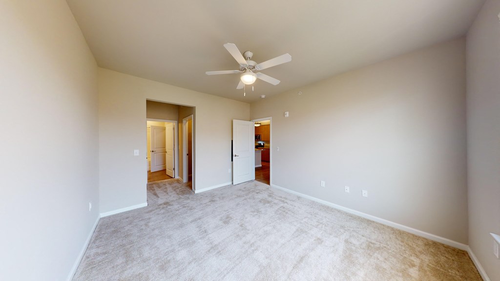 a spacious living room with a ceiling fan and white carpet