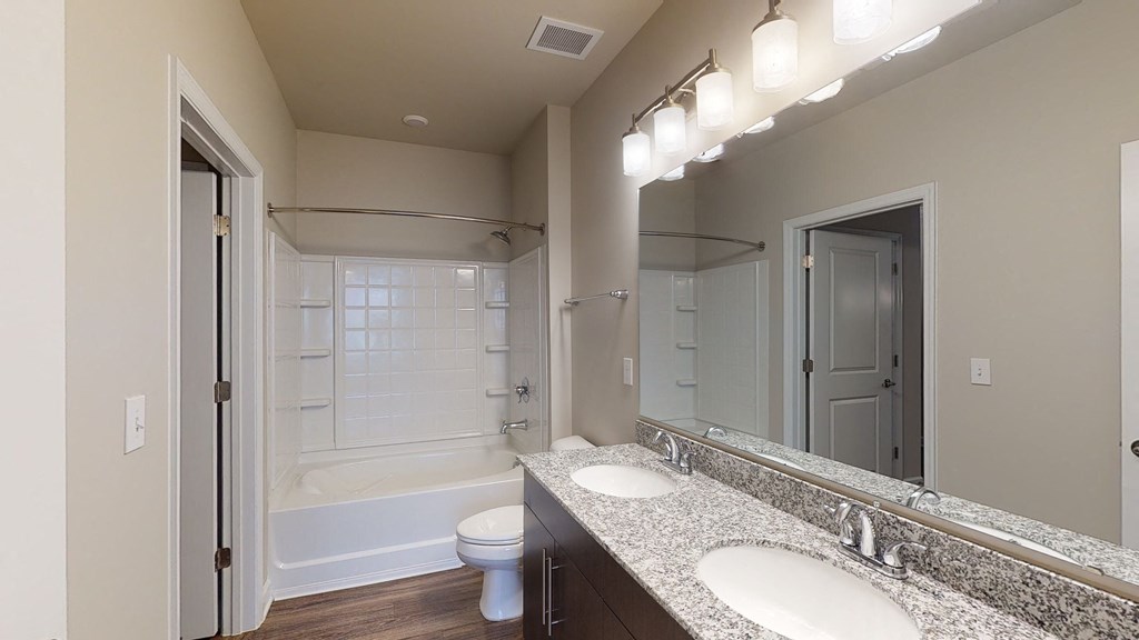 Bathroom with dual sinks, dark cabinets, toilet and shower with bathtub