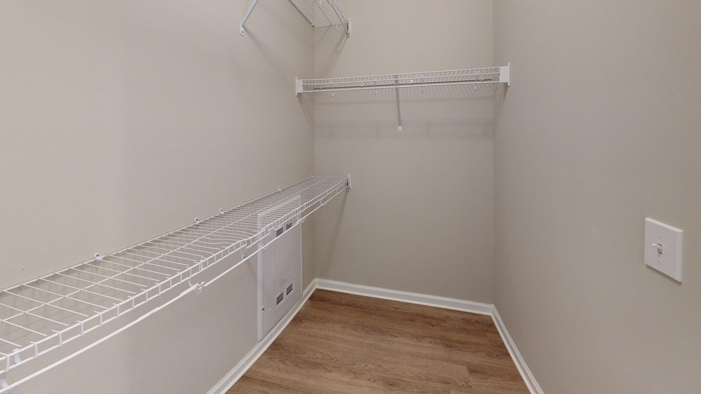 a walk in closet with a white closet shelf and a wood floor