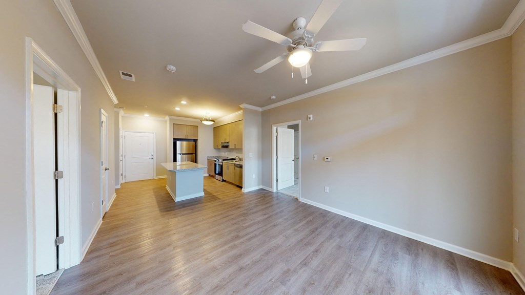 an empty living room with a ceiling fan and a kitchen