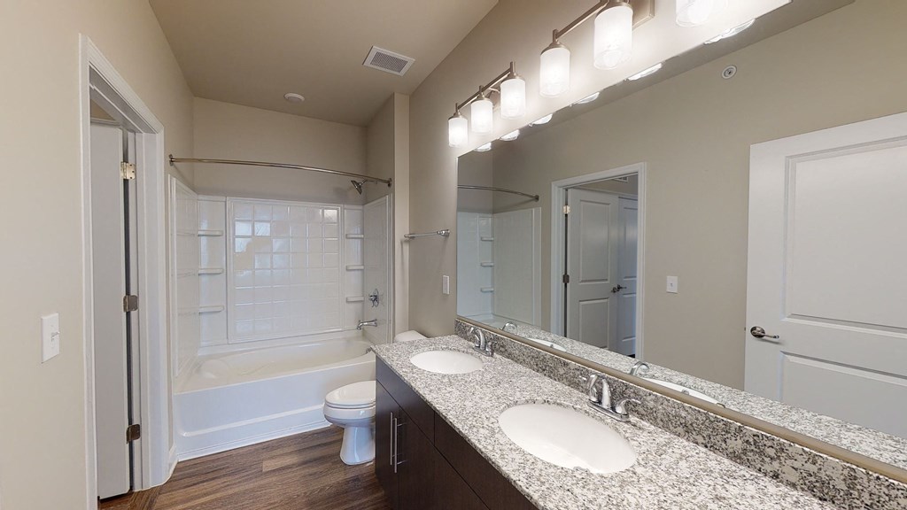 Bathroom with dual sinks, dark cabinets, toilet and shower with bathtub