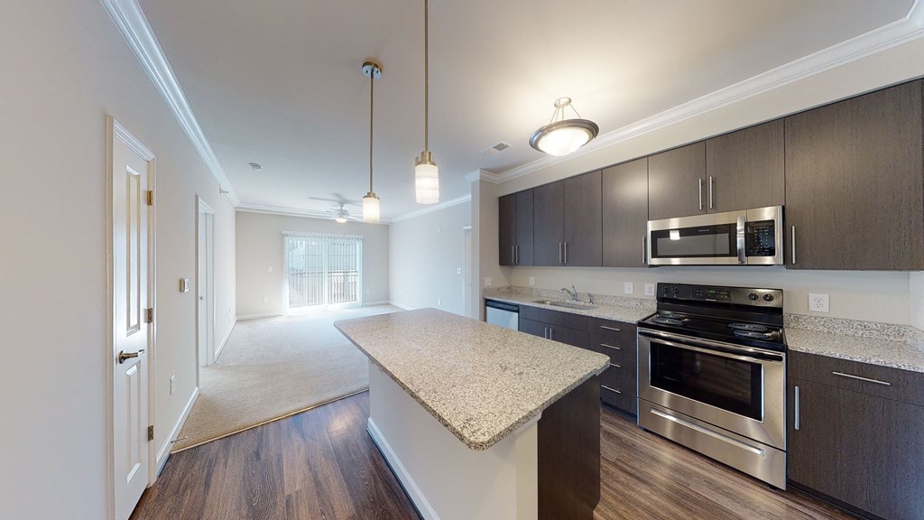 Kitchen with island, dark cabinets, vinyl floors and granite countertops; open to living room