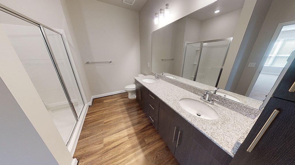 Bathroom with dual sinks, dark cabinets, toilet and walk-in shower