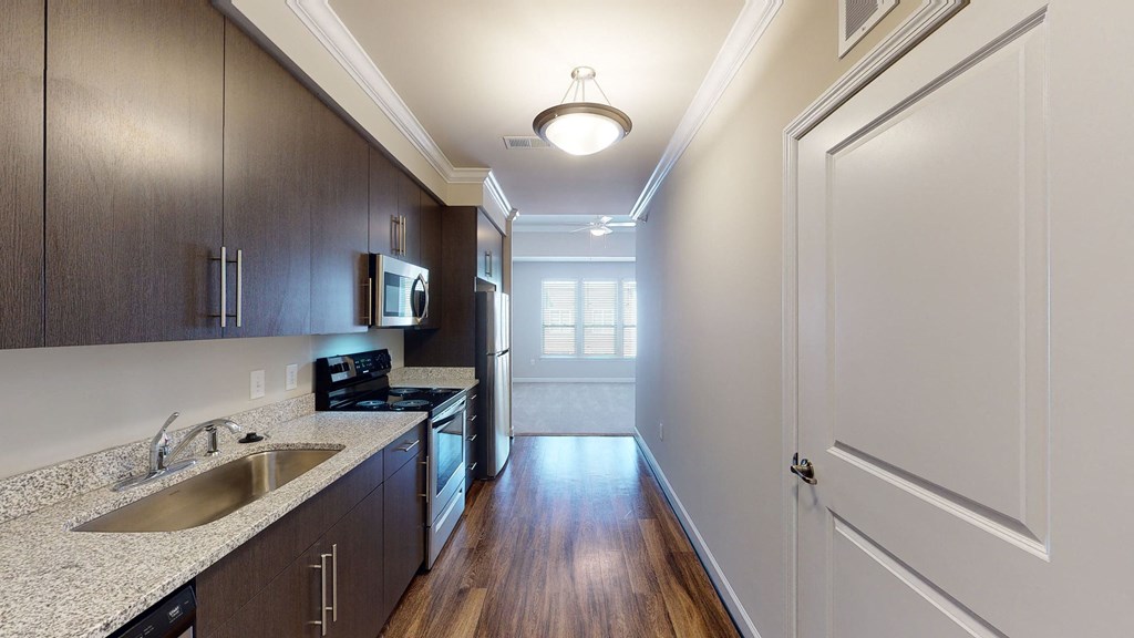 Kitchen with dark cabinets, granite countertops, vinyl wood plank floors; open to living room