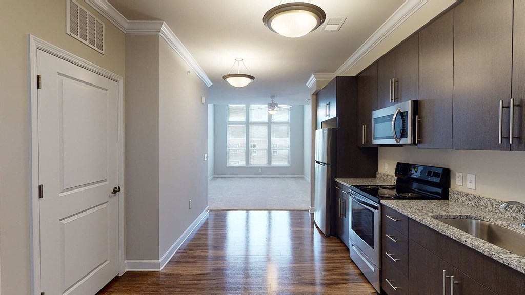 Kitchen with dark cabinets, granite countertops, vinyl wood plank floors; open to living room