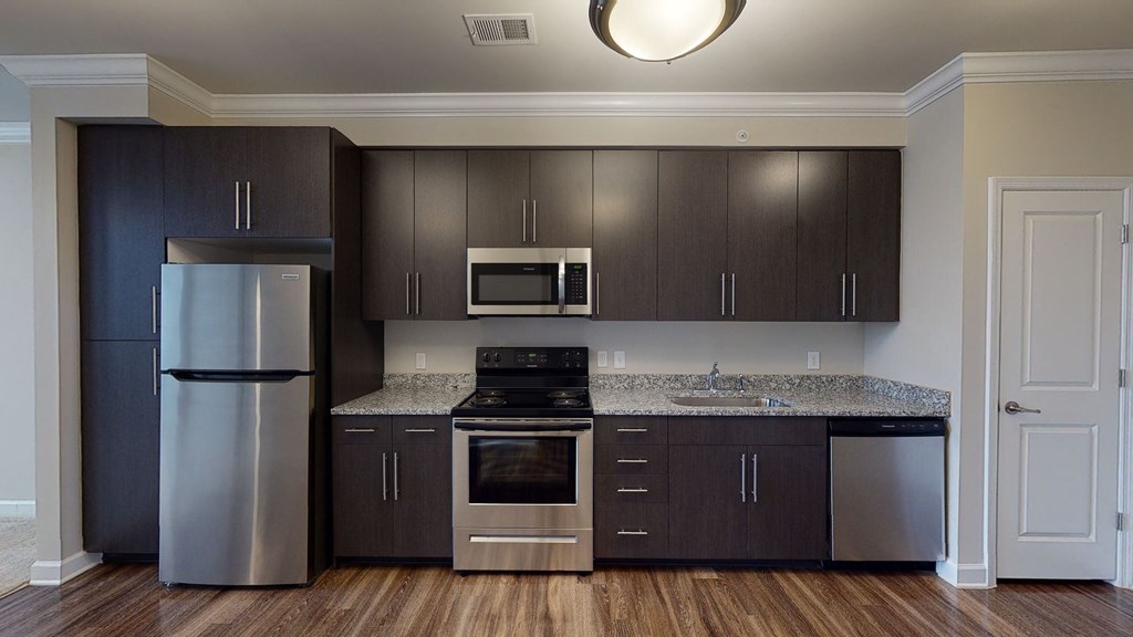 Kitchen with dark cabinets, granite countertops, vinyl wood plank floors; open to living room