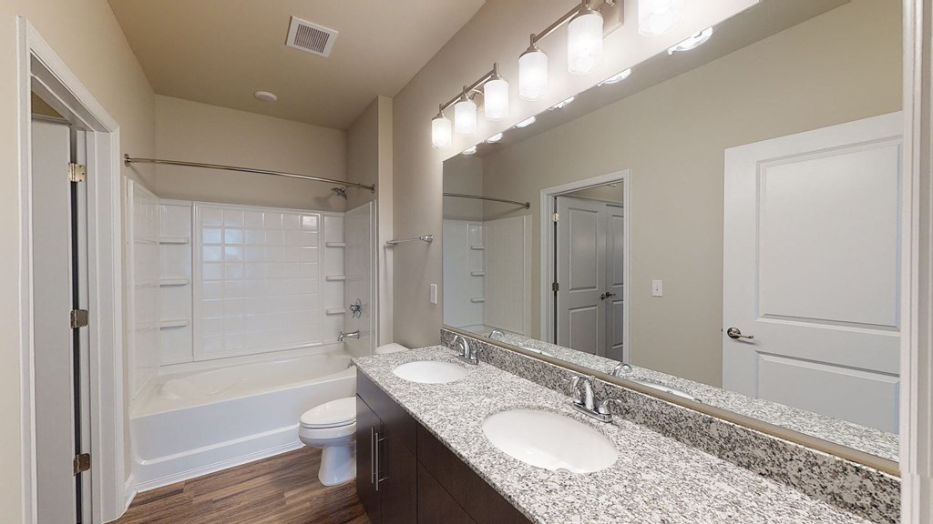 Bathroom with dual sinks, dark cabinets, toilet and shower with bathtub