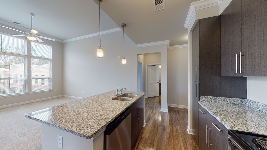 Kitchen with island, dark cabinets and granite countertops; open to the main living area with large windows