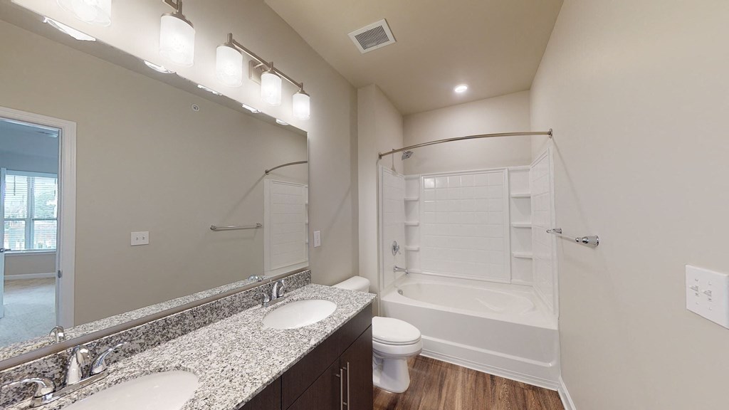 Bathroom with dual sinks, dark cabinets, toilet and shower with bathtub