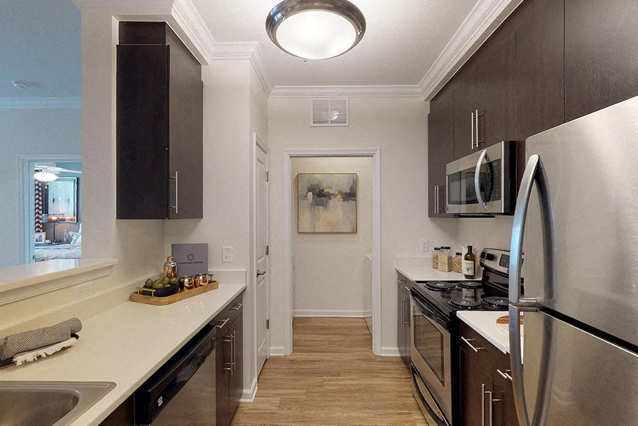 Kitchen with dark cabinets, quartz countertops, vinyl plank floors, stainless steel appliances; open to laundry room