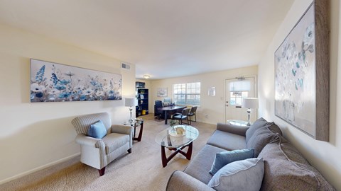 A living room with a grey couch and a painting on the wall.