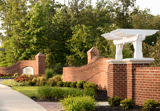 Community entrance with brick sign; road surrounded by trees