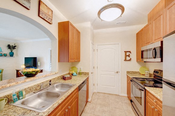 Galley-style kitchen with upgraded granite countertops and stainless steel appliances; door to washer/dryer room; open to living room