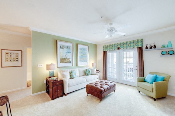 Living room with couch and chair; door to patio or balcony; bar seating at opening to the kitchen