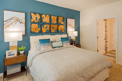 Pet-Friendly Luxury Apartments in Charlotte, North Carolina - Belmont at Tryon - Bedroom With Blue Accent Wall, Decorative Pillows, Matching Nightstands With Lamps, And Framed Wall Art.