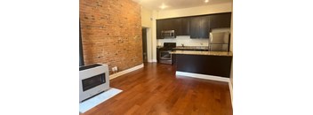 A kitchen with a brick wall and wooden floors.