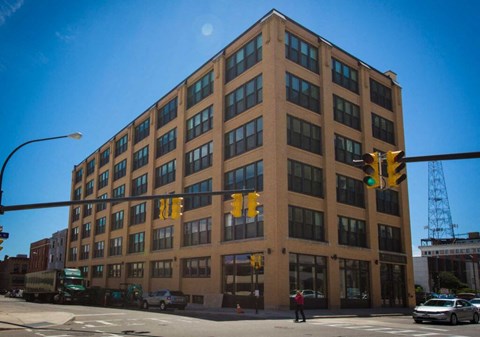 A large brown building with many windows is in the middle of a street.