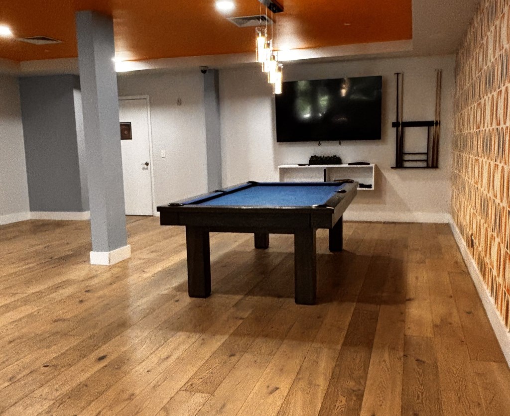 A pool table in a room with wooden flooring and a television mounted on the wall.
