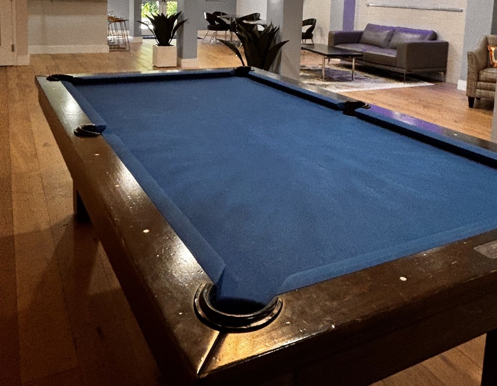 A pool table in a room with a couch and plants in the background.