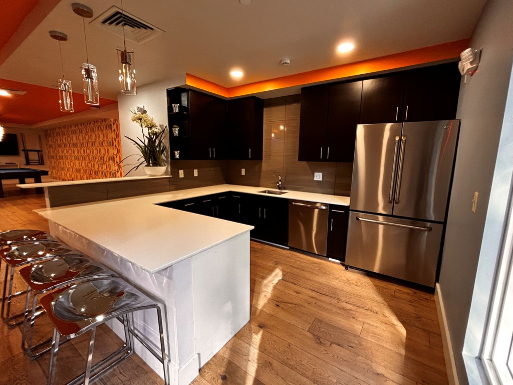 A kitchen area with three stools, a white countertop, and a stainless steel refrigerator.