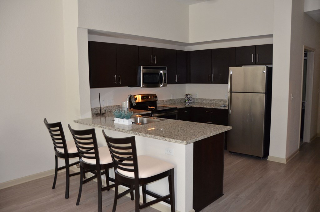 A kitchen with a white counter top and brown chairs.