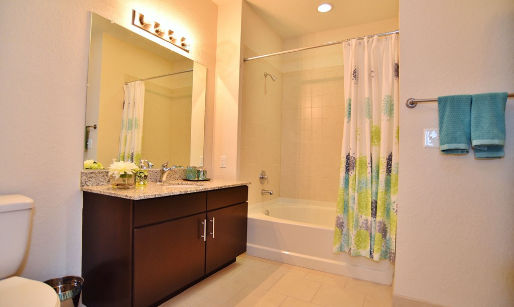 A bathroom with a white tub/shower, toilet, cabinet and mirror.