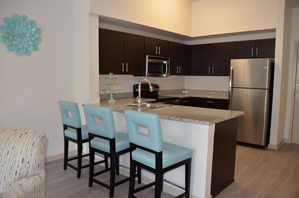 A kitchen with an island, three chairs, and a refrigerator.