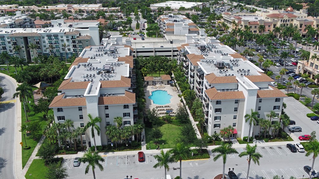 A large apartment complex with a pool in the middle of a courtyard surrounded by palm trees.