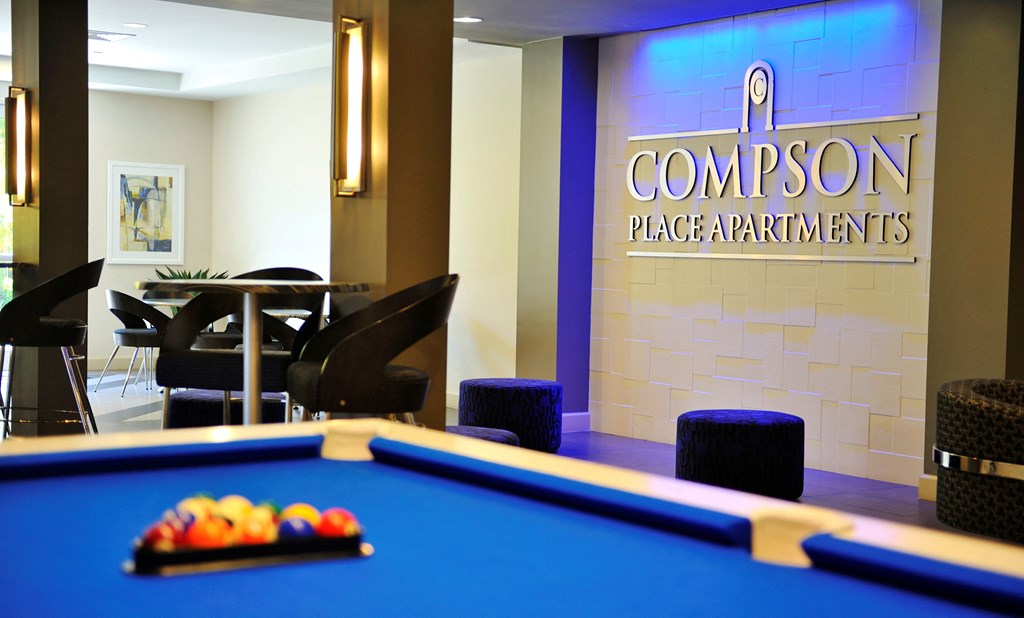 A pool table is in the middle of a room with a sign that says Compson Place Apartments.