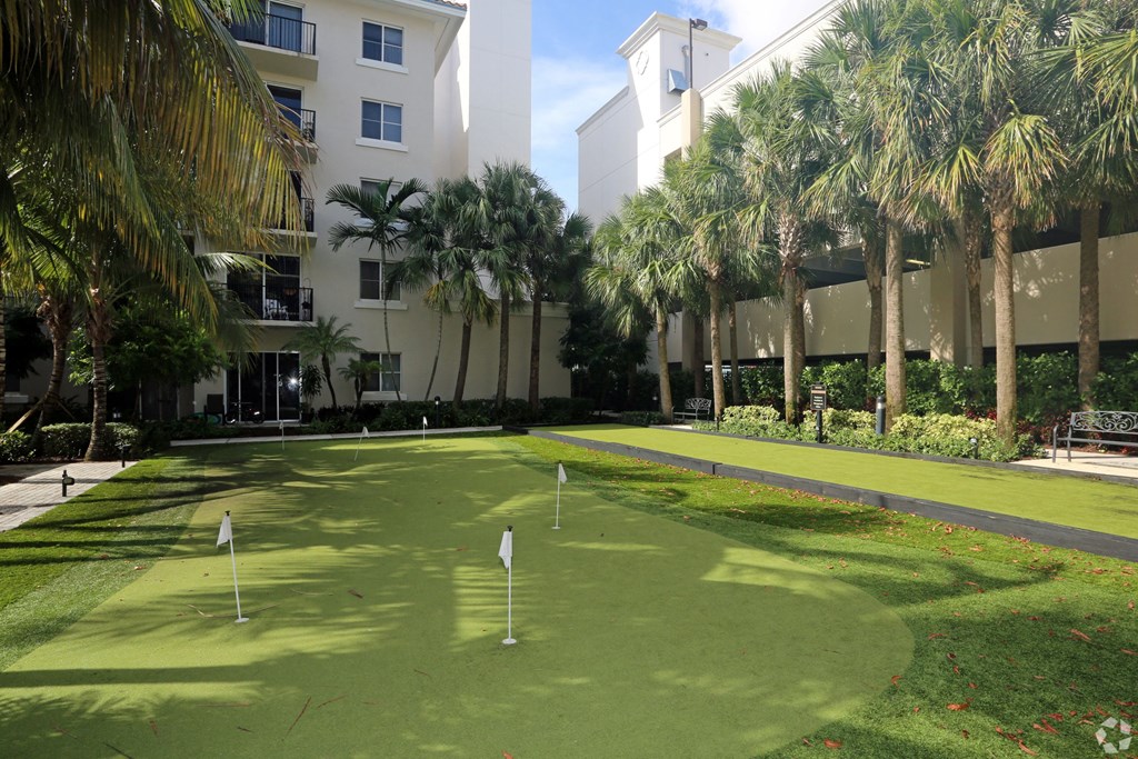 A putting green is surrounded by palm trees and a white building.