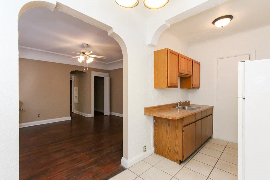 an empty living room with a kitchen with a sink and cabinets