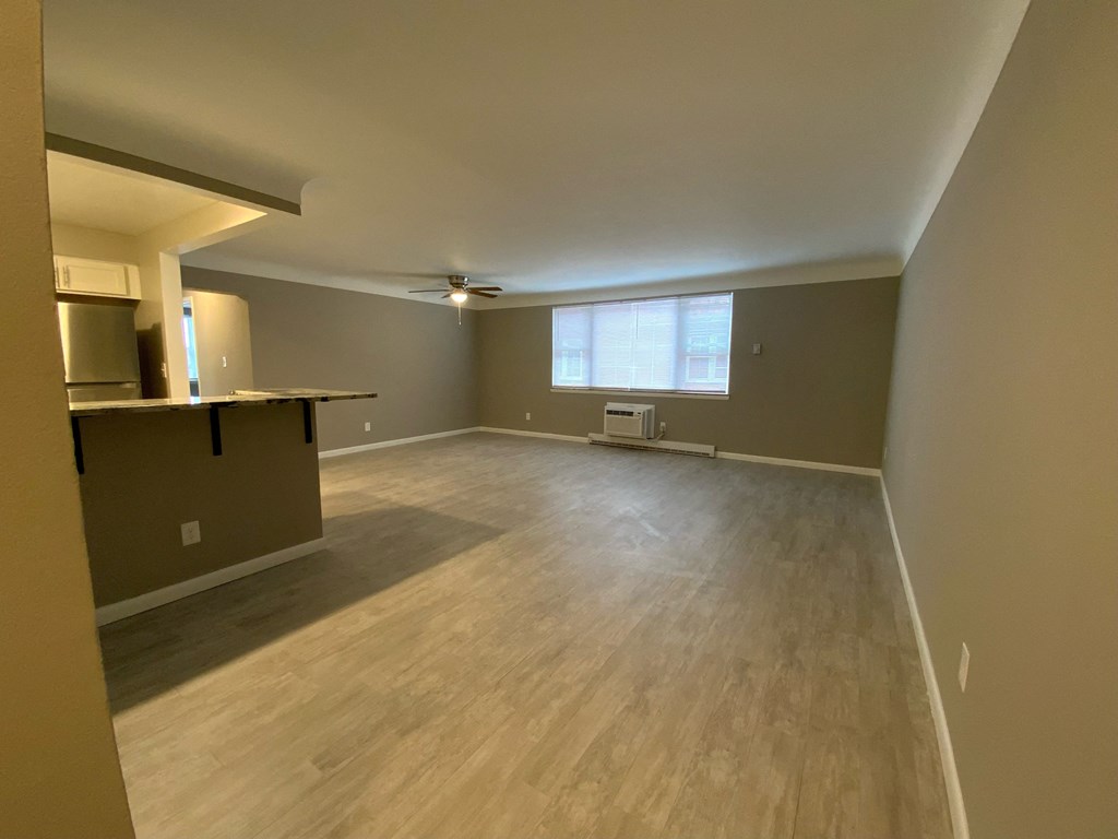 an empty living room with a kitchen and a window