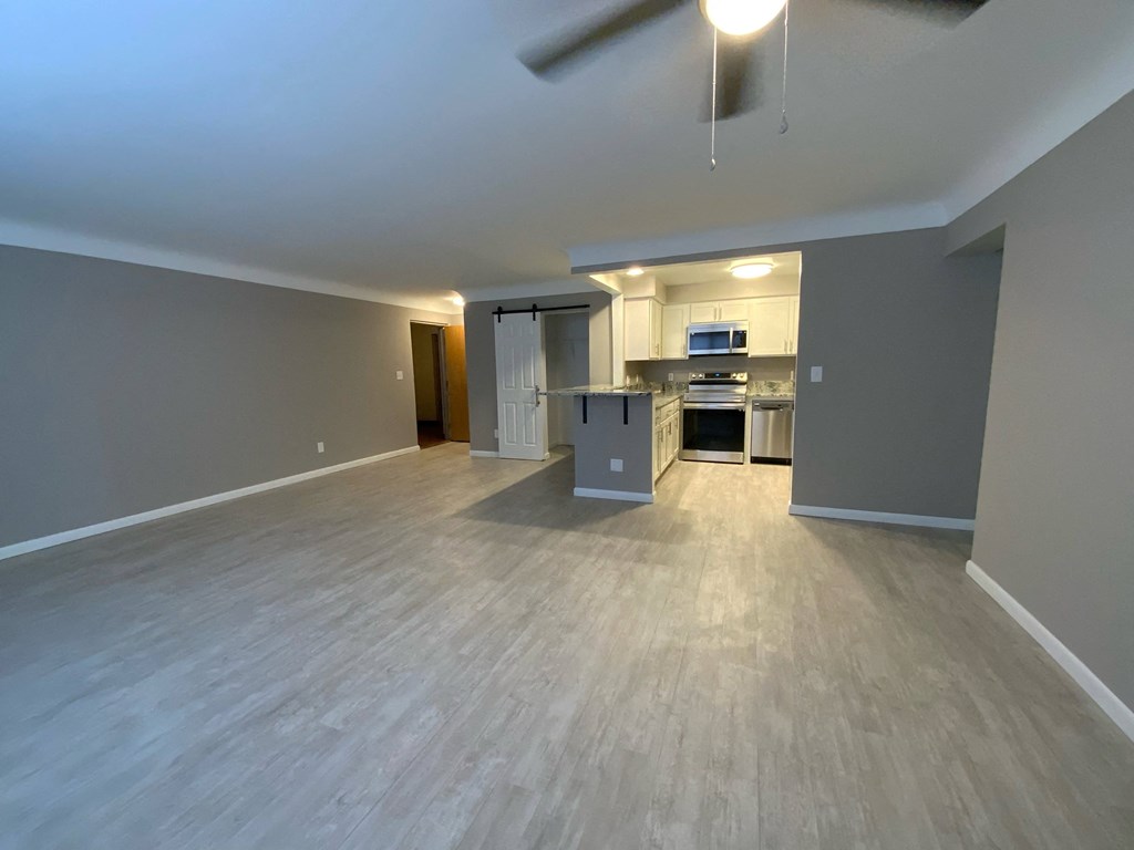 an empty living room with a kitchen and a ceiling fan