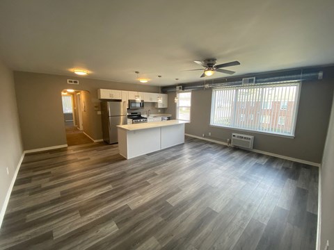 an empty living room with a kitchen and a ceiling fan