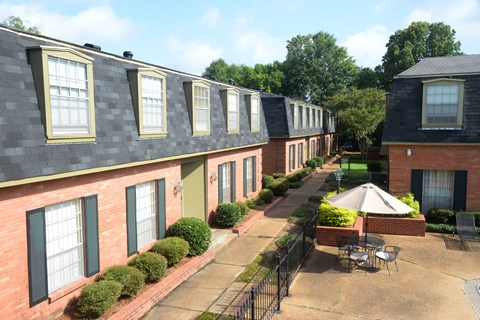 A sunny day at a brick apartment complex with a patio and a table.