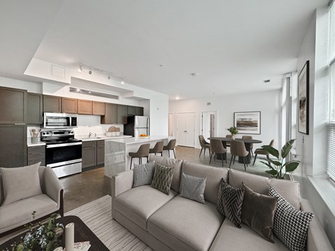 A modern living room with a grey sofa and a kitchen area in the background.