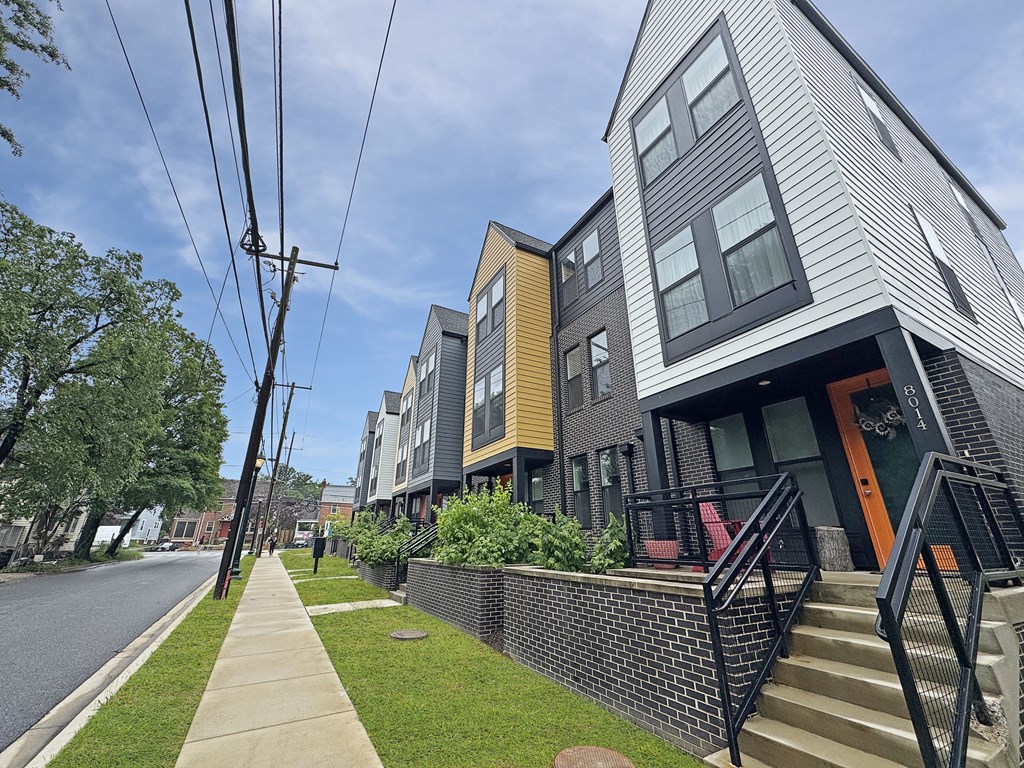 A modern two-story building with a grey and yellow exterior is situated on a street with a sidewalk and a metal fence.