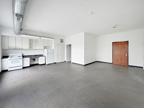 A large empty room with a kitchen area to the left.