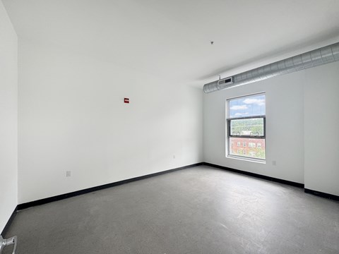A large empty room with a window and a fire extinguisher on the wall.