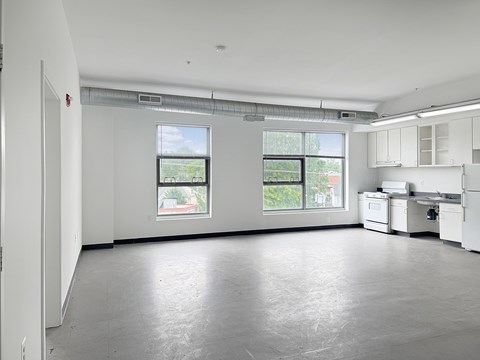 A large empty room with a kitchenette and two windows.