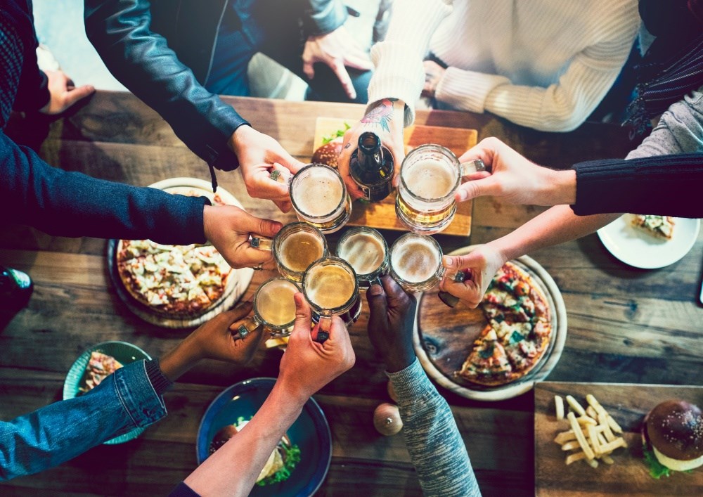 A group of people toasting with beer glasses at a table full of food.