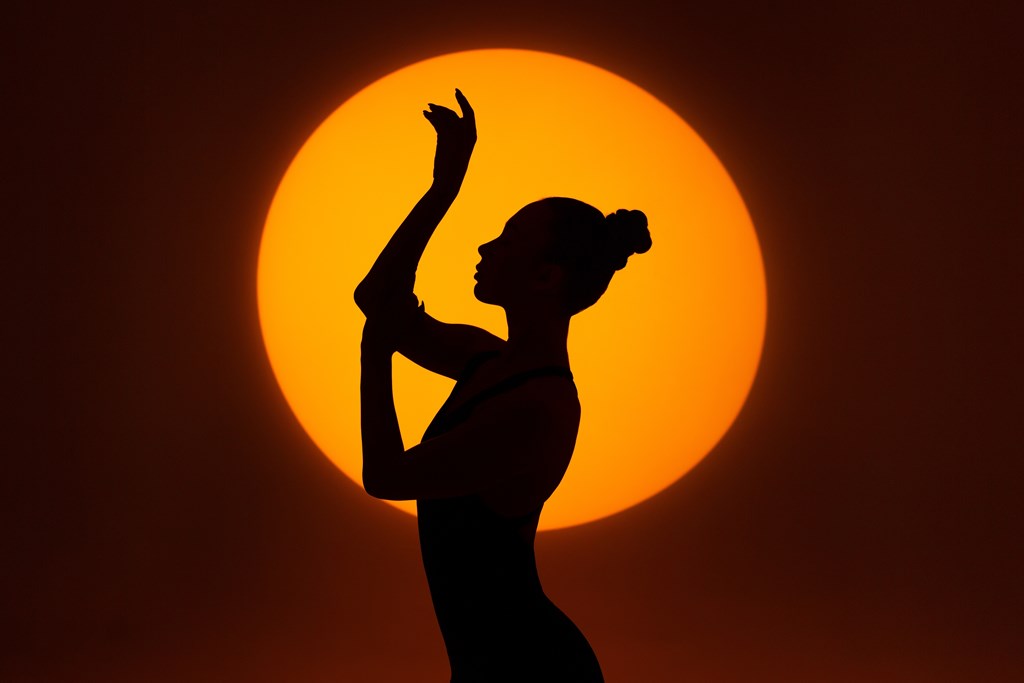 A silhouette of a person with a raised hand against a bright orange background.