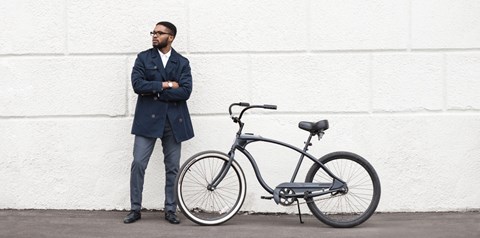 A man in a dark coat stands next to a black bicycle.