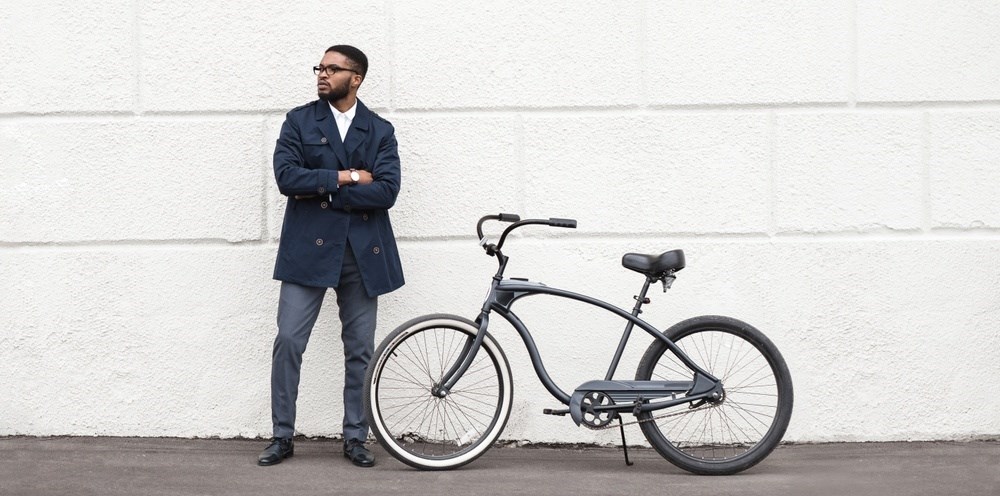A man in a dark coat stands next to a black bicycle.