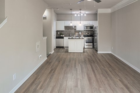 Open living room and kitchen with wood-look flooring, breakfast bar, and pendant lighting in a one-bedroom apartment at The Brownstones in Far North Dallas