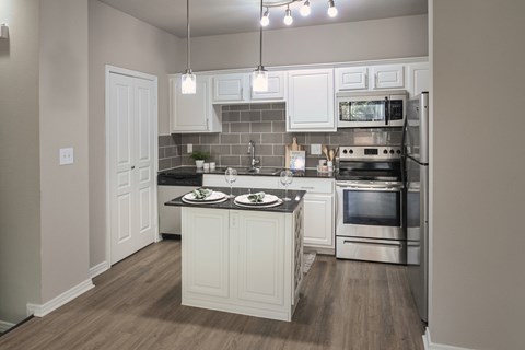 Kitchen with white cabinets, stainless steel appliances, tile backsplash, and center island in a one-bedroom apartment at The Brownstones