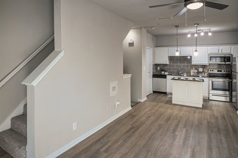 Open living area with staircase and view into the kitchen with island and stainless steel appliances in a one-bedroom apartment with direct access 1-car garage